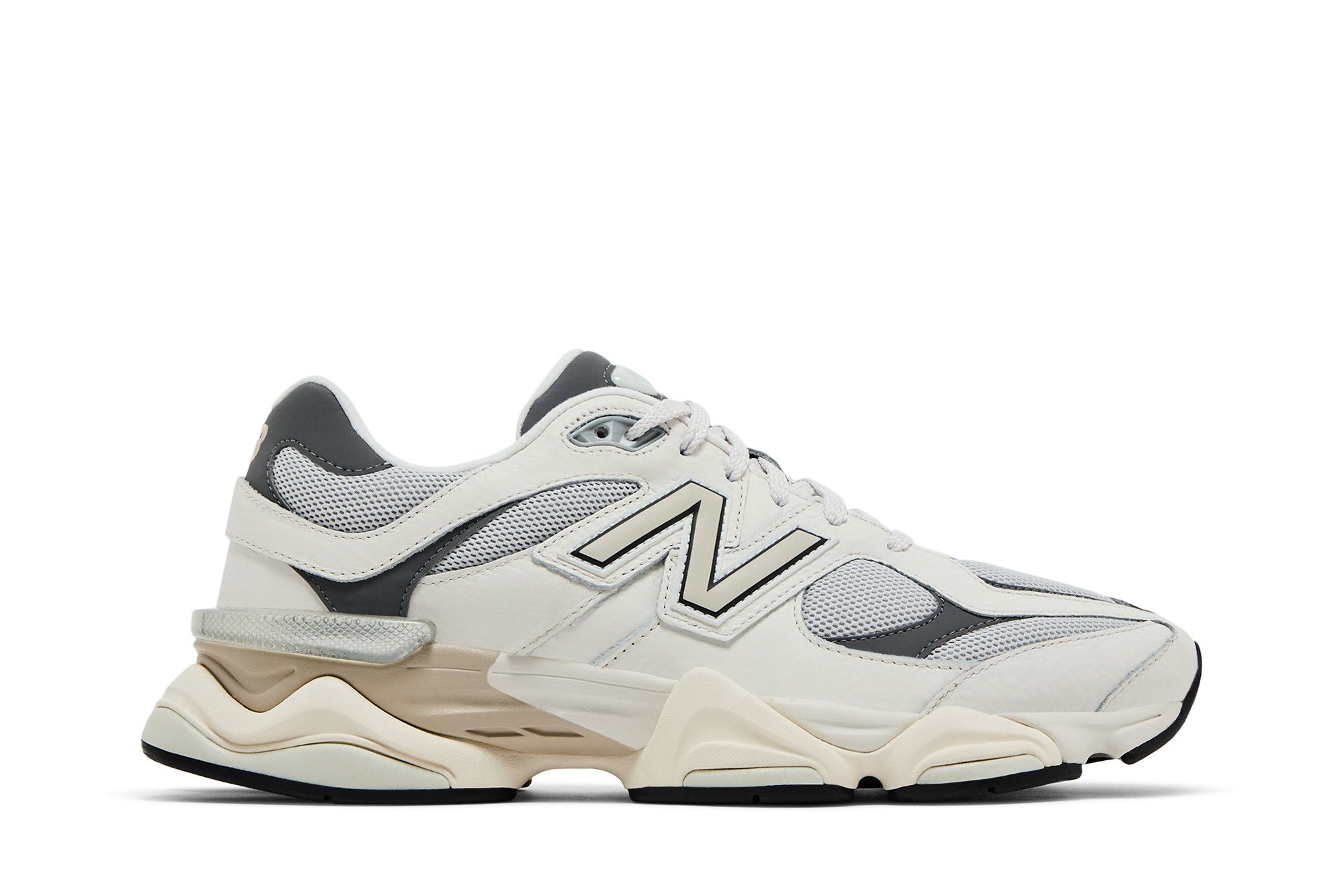 Imagem da lateral externa de um tênis esportivo New Balance modelo 9060 'Grey Day 2025'. O calçado apresenta uma combinação de cores cinza, branco, bege e preto.