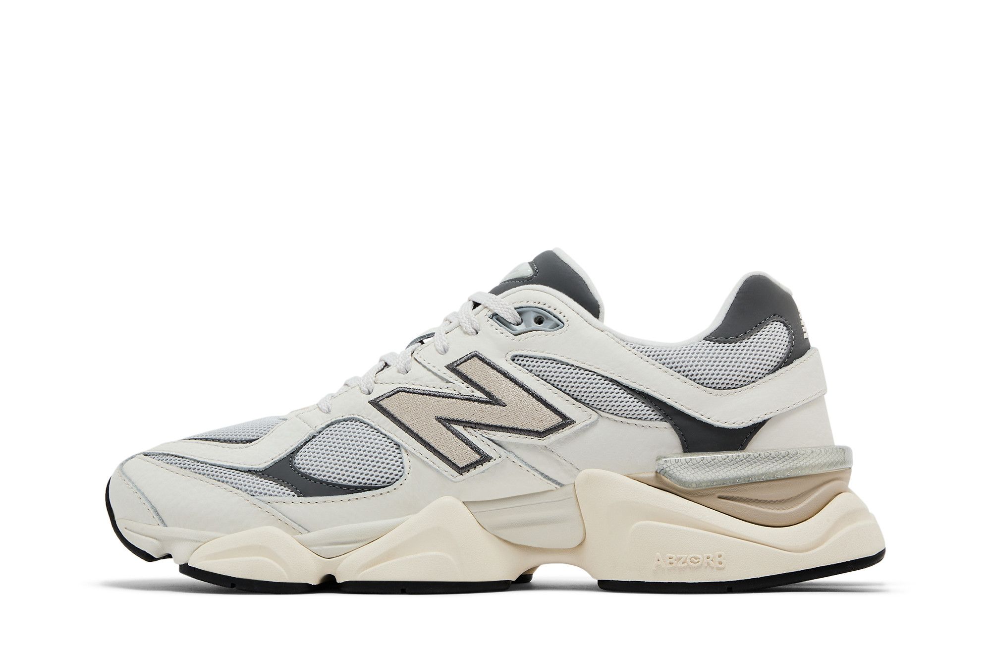 Imagem da lateral interna do tênis New Balance modelo 9060 'Grey Day 2025'. O tênis é apresentado em cores cinza claro, branco e bege.