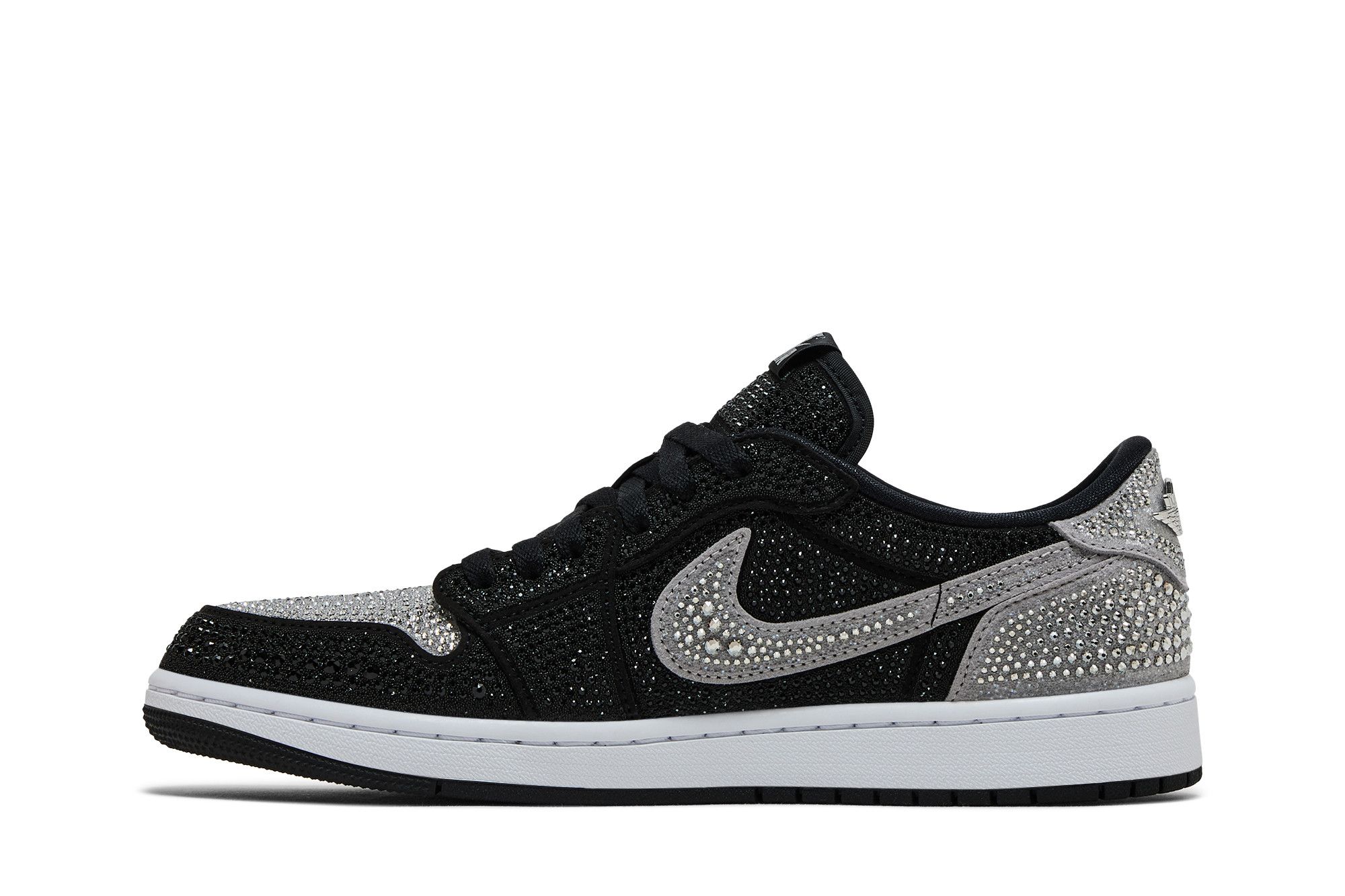 Imagem lateral direita do tênis Swarovski x Wmns Air Jordan 1 Retro Low OG 'Shadow' com fundo branco. O tênis é detalhado com cristais Swarovski que cobrem as áreas cinza do calçado, incluindo o swoosh, bico, e calcanhar, contrastando com as partes pretas não brilhantes. O tênis está posicionado para destacar o design luxuoso e a colaboração exclusiva de marcas de alta moda e streetwear.