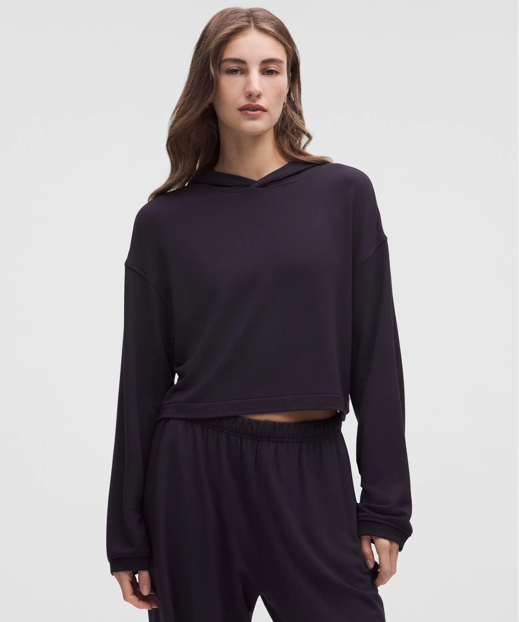 Imagem frontal de uma mulher usando um moletom preto BeCalm Hoodie com capuz, tecido ultra-suave, corte casual e comprimento cropped. Ela está olhando para a frente com expressão neutra, fundo branco.